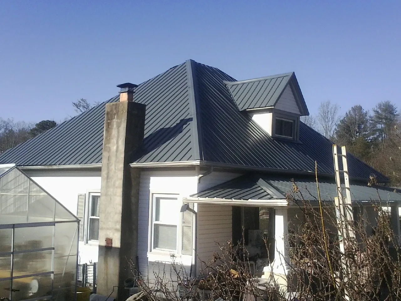 Dark blue standing seam metal roof on a white farmhouse with dormer — Slate & Tile Roof Repair by Roofing Brothers in War