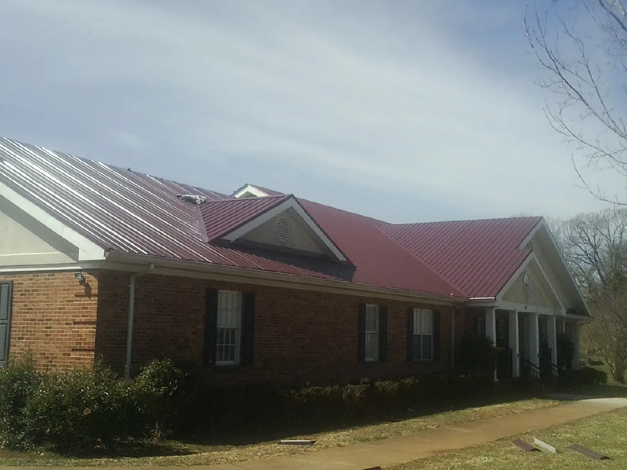 Red metal roof with gabled entries on a long brick building, from a Hail Damage Roof Repair job in War