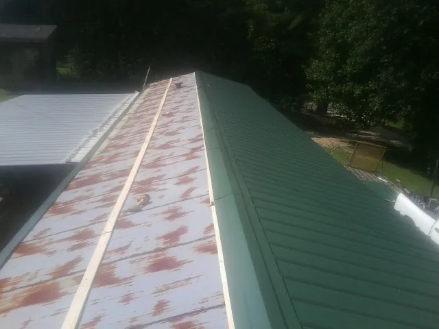 Old rusted panels beside newly installed green metal roofing — Wind Damage Roof Repair by Roofing Brothers in War