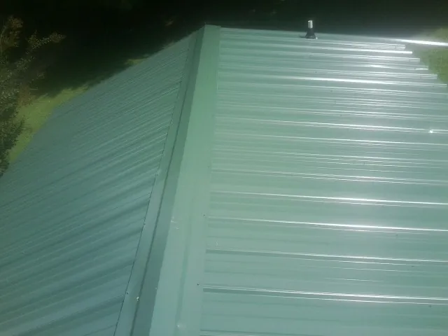 New green metal panels meeting at the ridge of a roof — Flat Roof Repair work by our crew in War