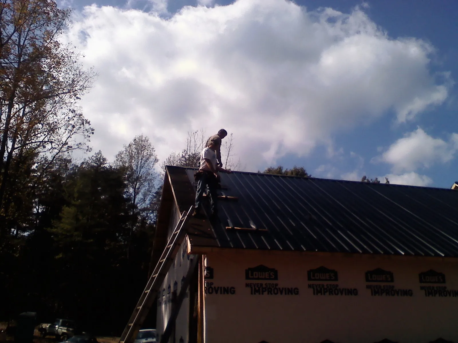 Roofer fastening dark metal panels high against a cloudy sky, from a Roof Inspection job in War