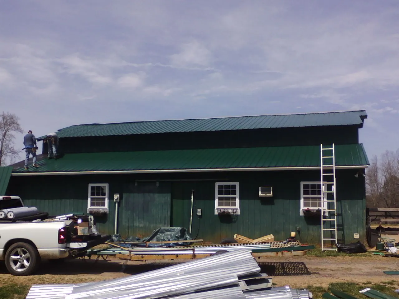 Crew installing green metal roofing on a large green barn in War