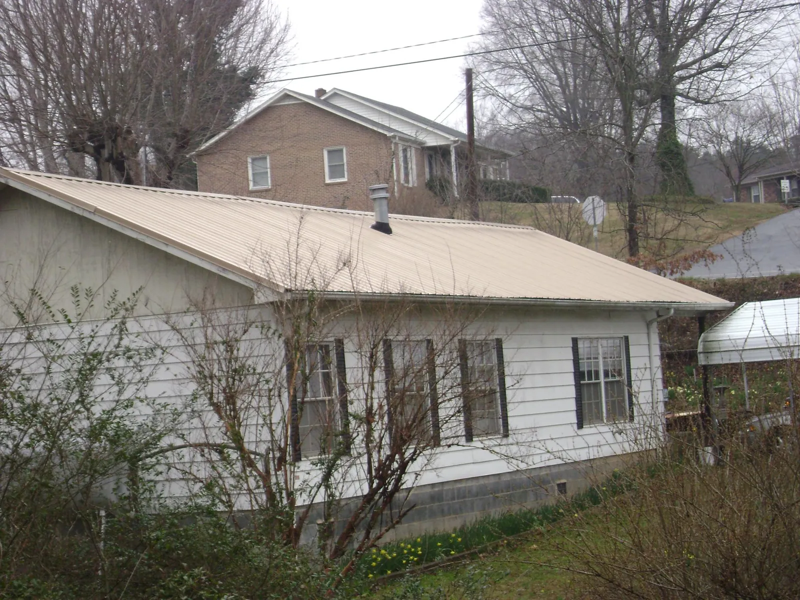 Tan metal roof on a white sided house set into a hillside — Commercial Roofing by Roofing Brothers in War